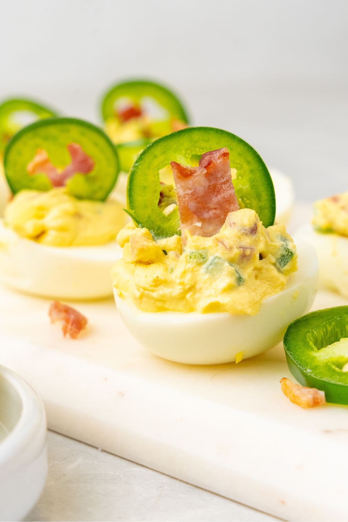 Close up of two jalapeno popper deviled eggs on a white cutting board.