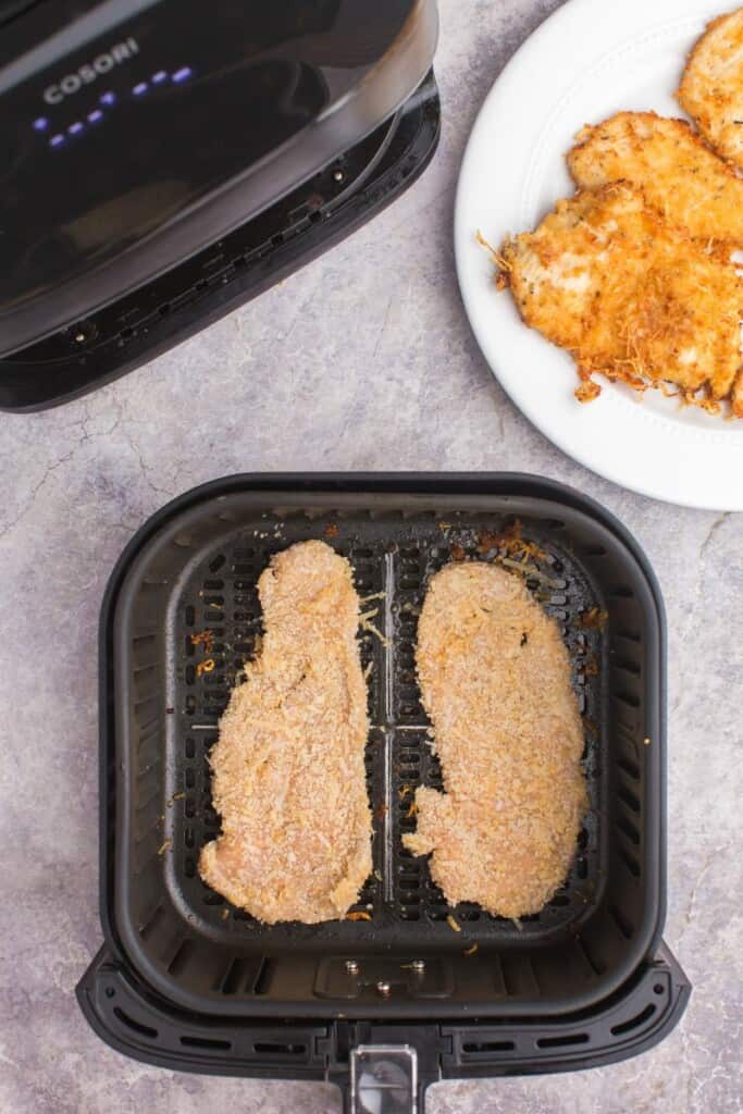 adding coated chicken breasts to an air fryer basket 
