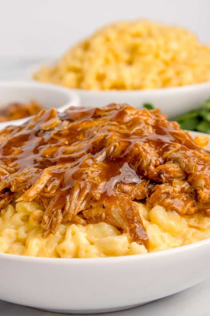 adding a spoonful of pulled pork on top of macaroni and cheese 
