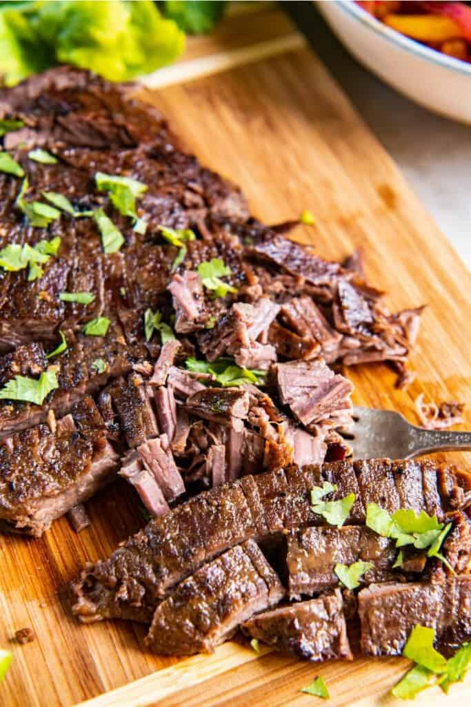 shredding flank steak on a wooden cutting board