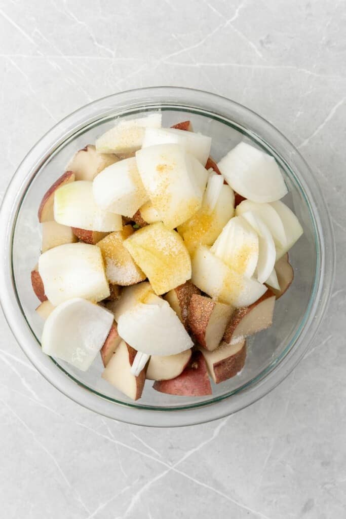 Potatoes and onions in a bowl mixed with oil and seasonings