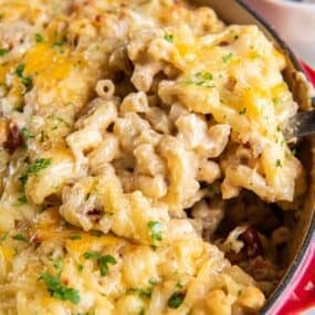 Dutch oven mac and cheese in a dutch oven pot being scooped up by a serving spoon so you can see the cheesiness and bacon.