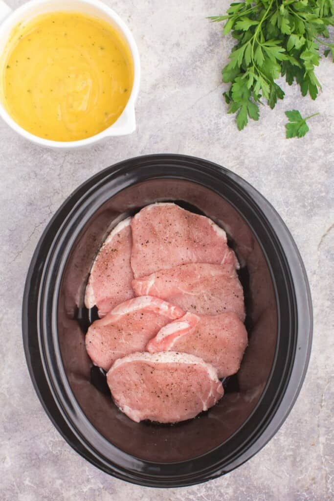 Seasoned pork chops in the bottom of a crockpot.