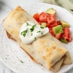 Air fried chimichanga served with sour cream and chunks of tomato and avocado.