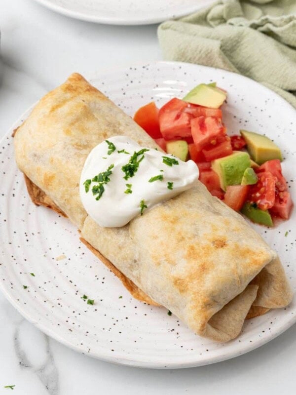Air fried chimichanga served with sour cream and chunks of tomato and avocado.