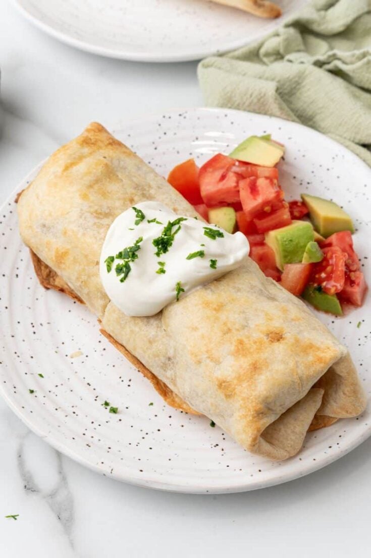 Air fried chimichanga served with sour cream and chunks of tomato and avocado.