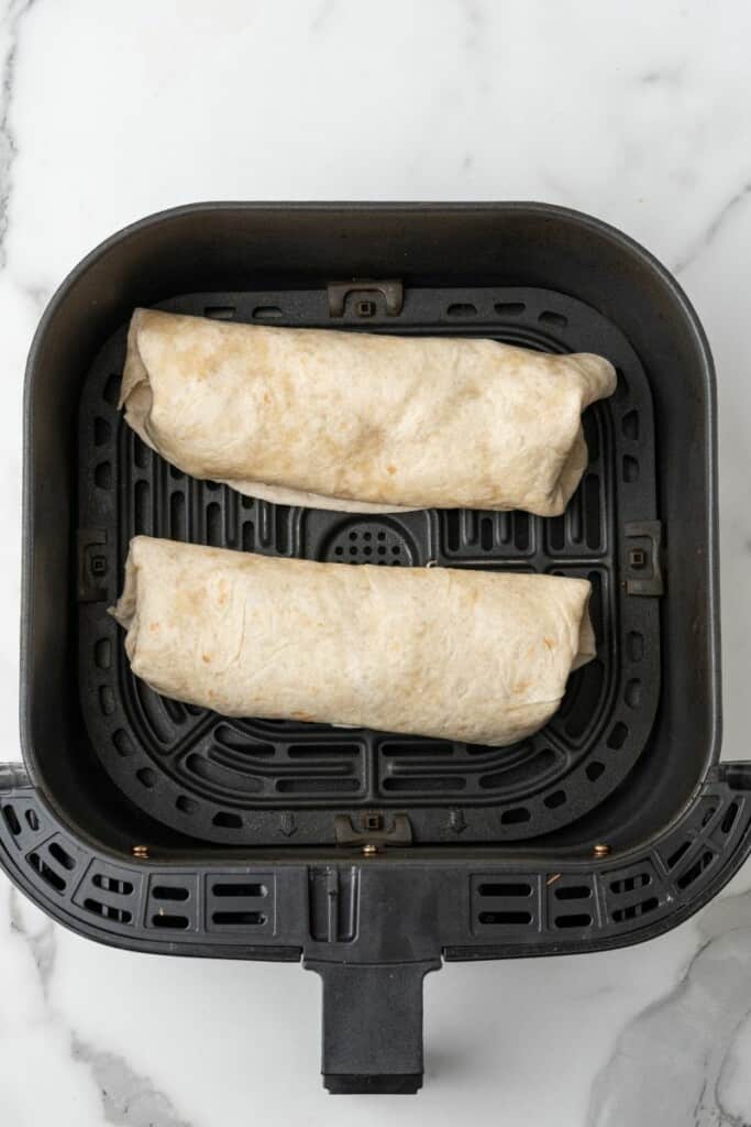 Two chimichangas in air fryer basket.