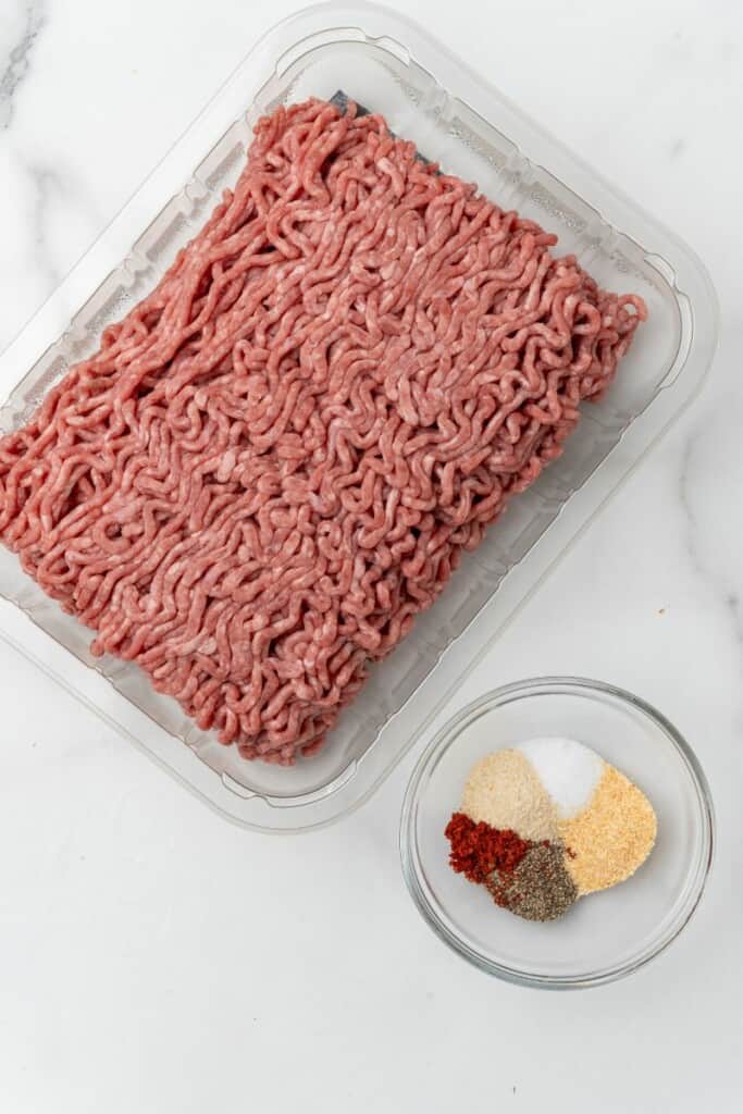 Raw beef in packaging next to small bowl of seasoning blend.