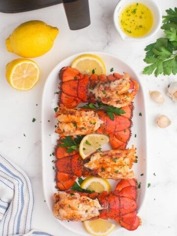 Air fried lobster tails lined up on a platter with garnish.