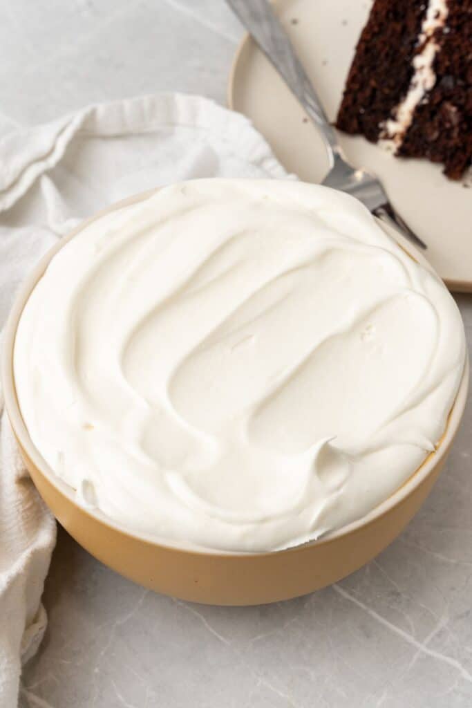Cool whip frosting in a large bowl next to a chocolate cake.