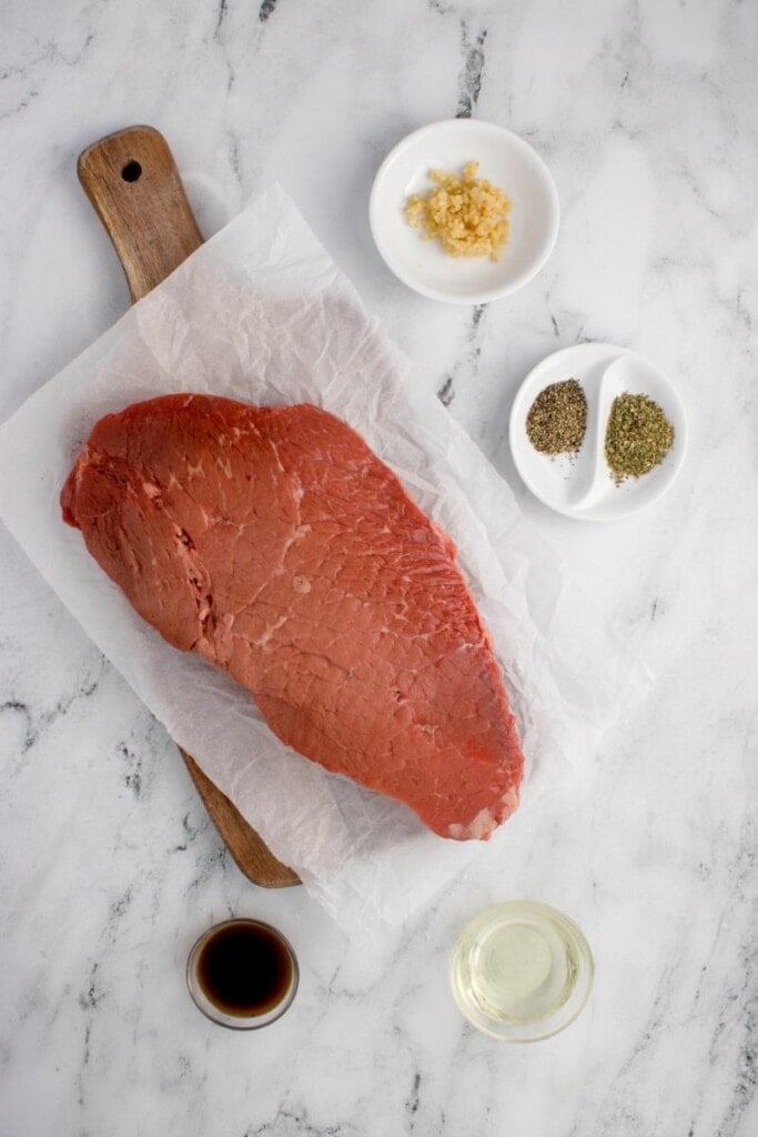 Raw cut of top round beef next to seasonings.