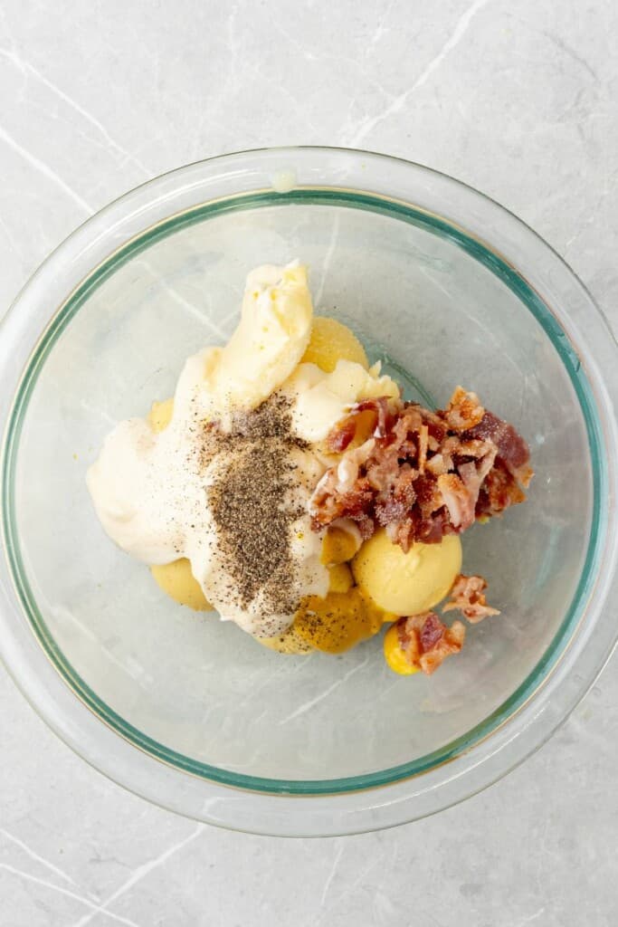 adding ingredients for deviled egg filling to glass bowl 