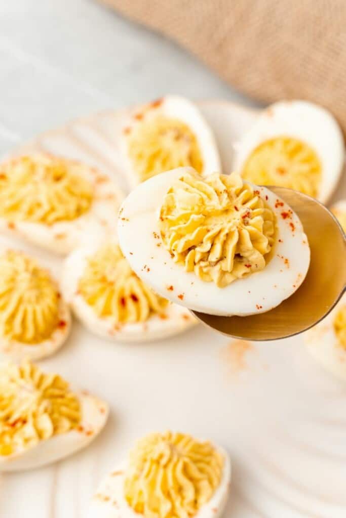 scooping up a deviled egg topped with crispy bacon 