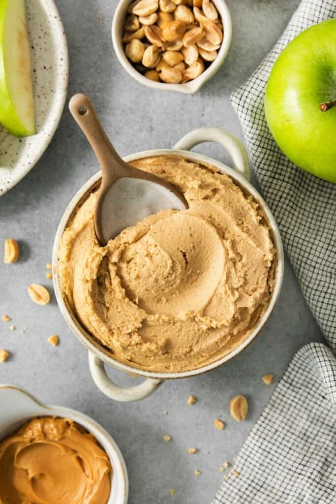 Bowl of peanut butter dip with green apples and peanuts.