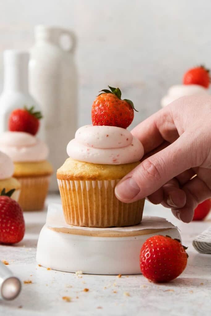 adding a fresh strawberry on top of strawberry cream cheese frosted cupcake 