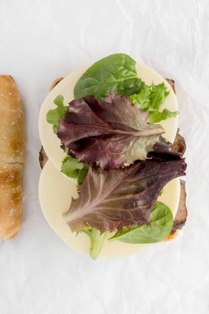 Adding greens to cheese and beef sandwich recipe.