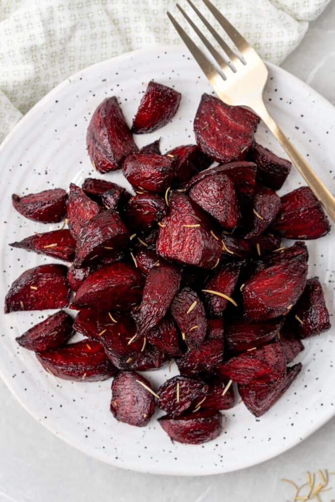 Roast beets cooked in an air fryer on a white plate with a fork next to it.
