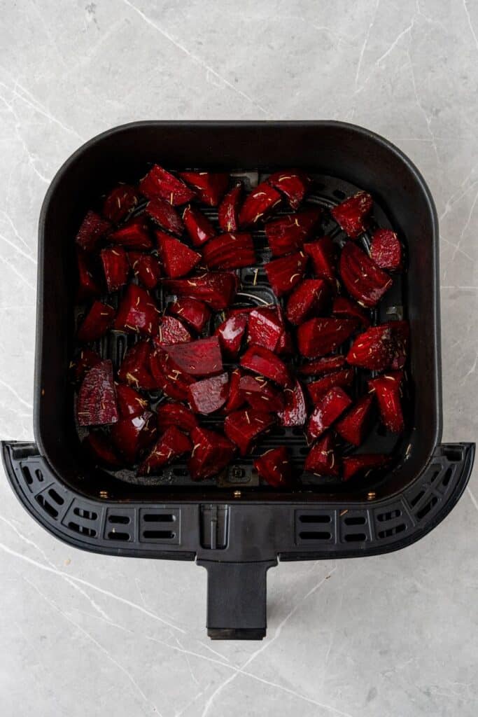 Raw red beets in an air fryer basket about to be cooked.
