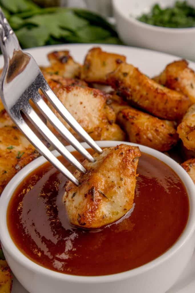 Air fryer chicken bites being dipped into BBQ sauce with a fork.