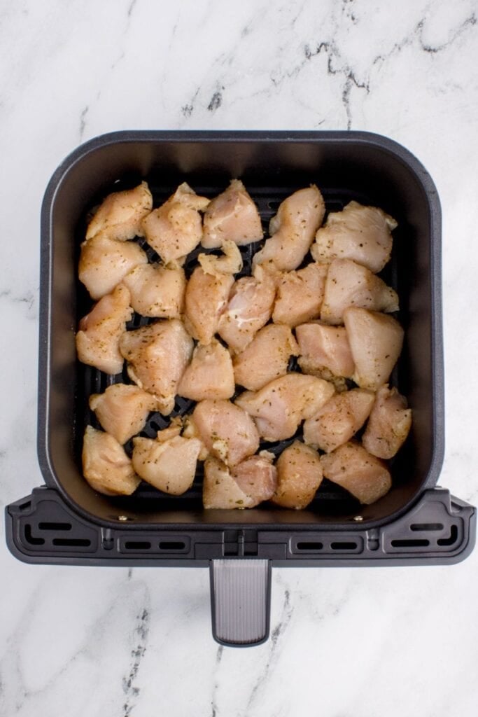Raw chicken bites in an air fryer basket about to air fried.