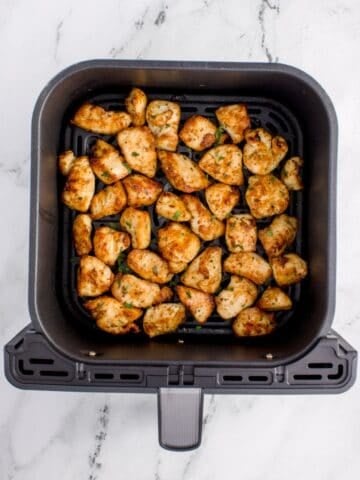 Cooked chicken bites in an air fryer basket.