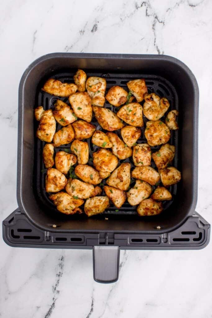 Cooked chicken bites in an air fryer basket.