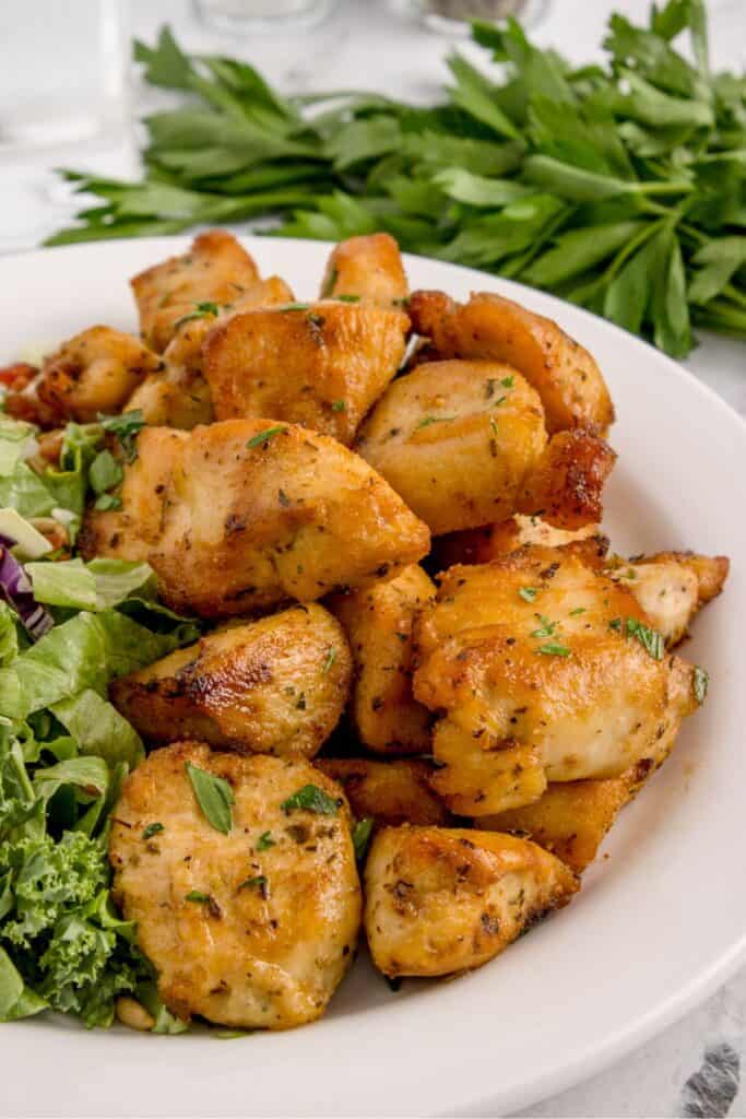 Air fryer chicken bites on a plate served next to a salad.