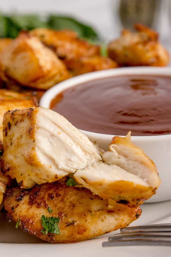 Close up of air fryer chicken bites with one broken open to see the chicken breast meat inside.