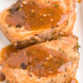 Instant pot pork chops close up on a white plate covered with the gravy from the pot.