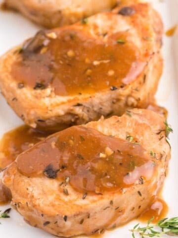 Instant pot pork chops close up on a white plate covered with the gravy from the pot.