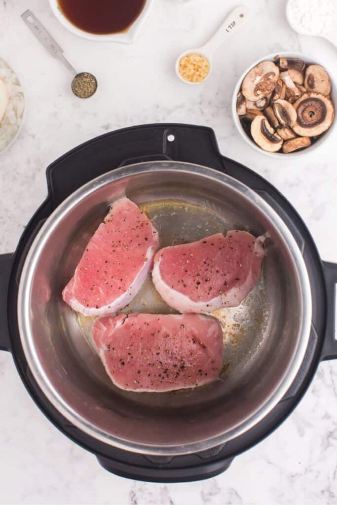 Raw pork chops in the pressure cooker getting sauteed.