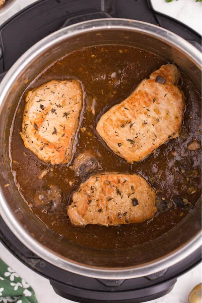 Instant Pot pork chops still sitting in the pressure cooker surrounded by the gravy.
