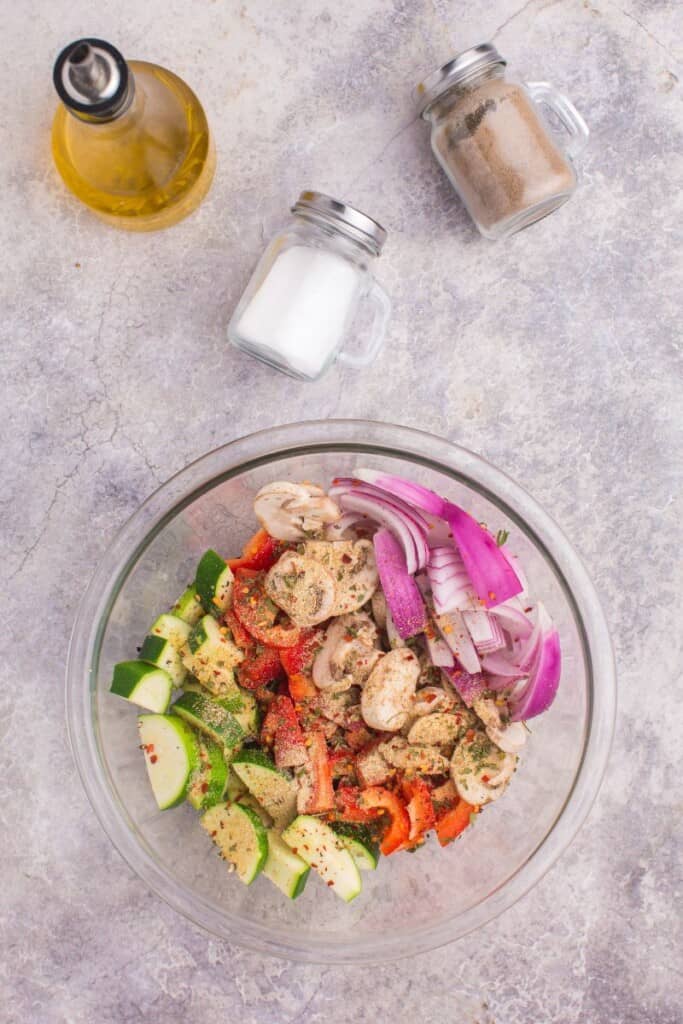 adding spices to sliced veggies in a glass bowl 