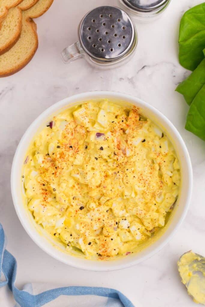 overhead shot of egg salad in a bowl seasoned with black pepper and paprika.