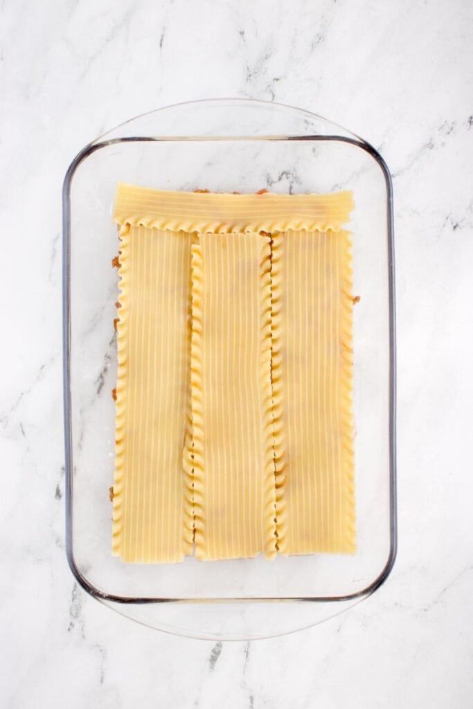 adding lasagna noodles over the layer of meat sauce in a glass pan.