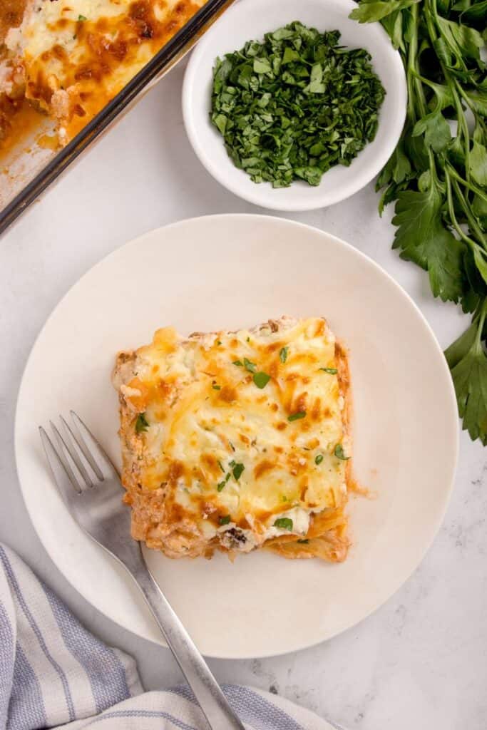 a slice of cheese lasagna on a plate topped with parsley