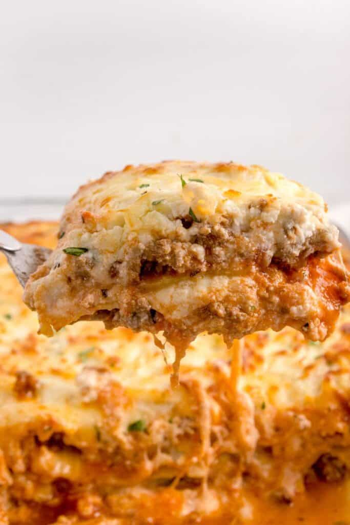 cutting up a slice of cheesy lasagna with a spatula 