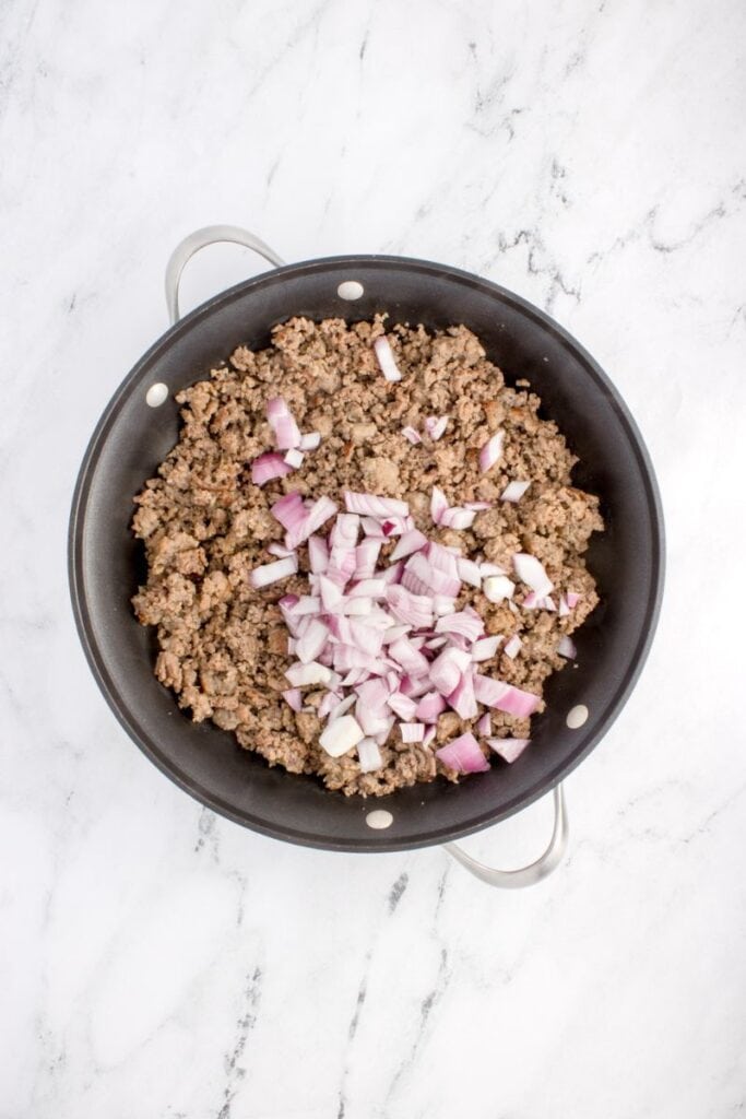 adding red onions to cooked ground beef in pan.