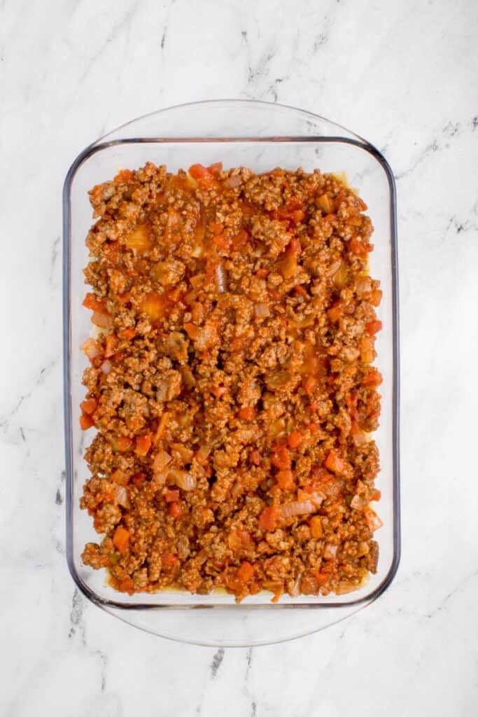 adding the first layer of tomato meat sauce to a lasagna baking pan.