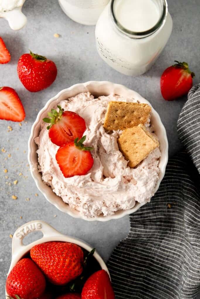 bowl of cream cheese based dip with sliced berries and graham crackers on top