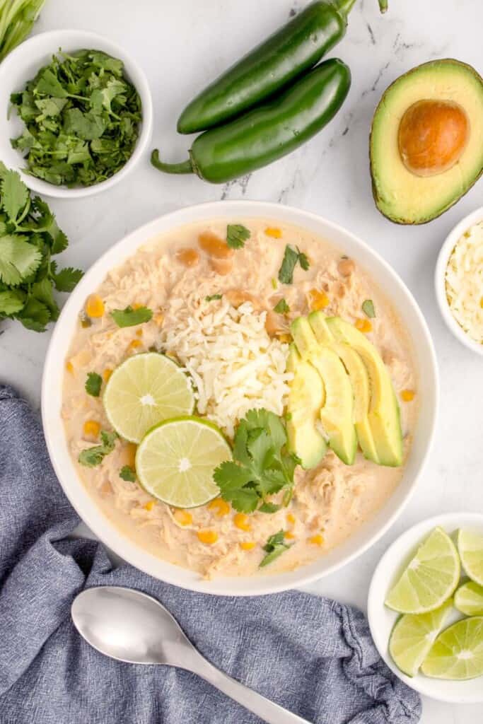 chicken chili made with cream cheese in a bowl surrounded by avocado and jalapenos. 