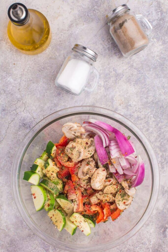 Vegetables mixed in a bowl with seasoning and oil.