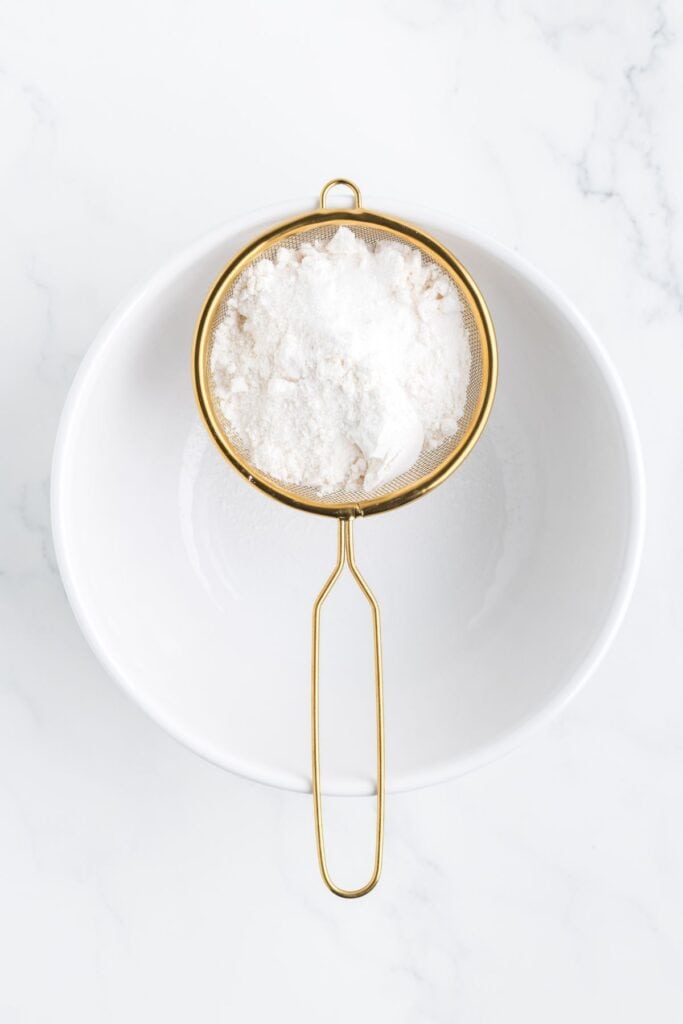 sifting flour and powdered sugar with a softer into a bowl 