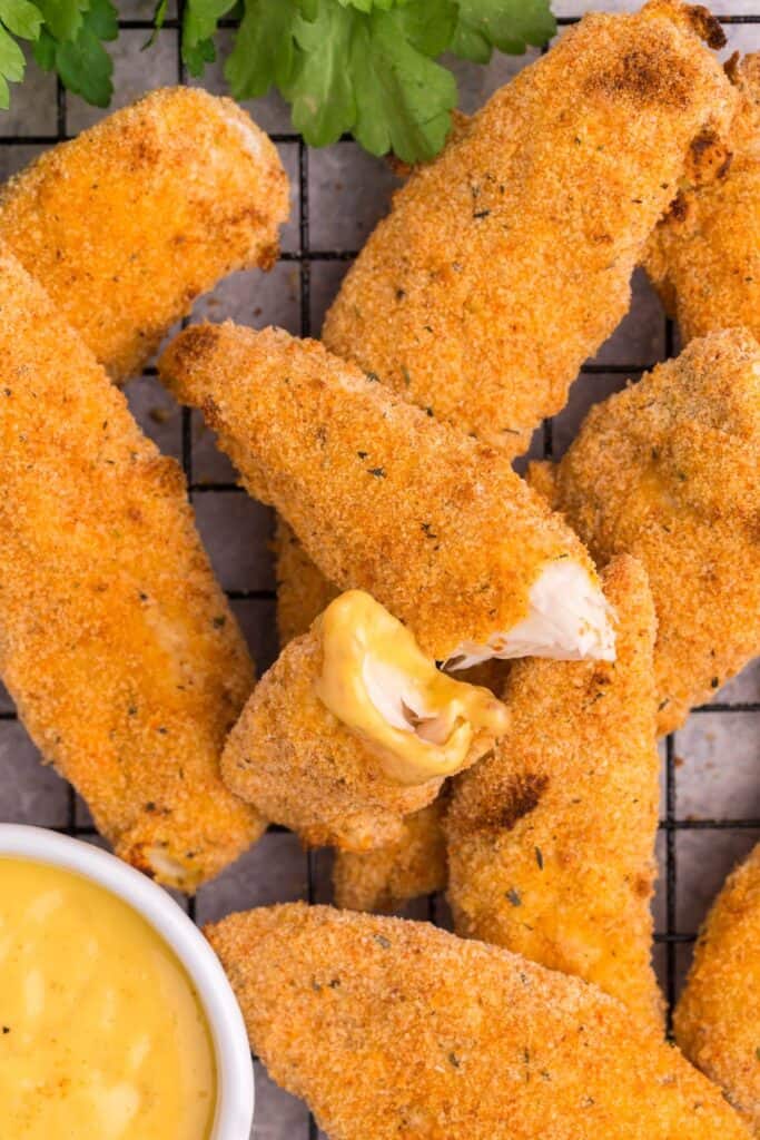 close up of chicken tenders with one broke in half with a little honey mustard on the end