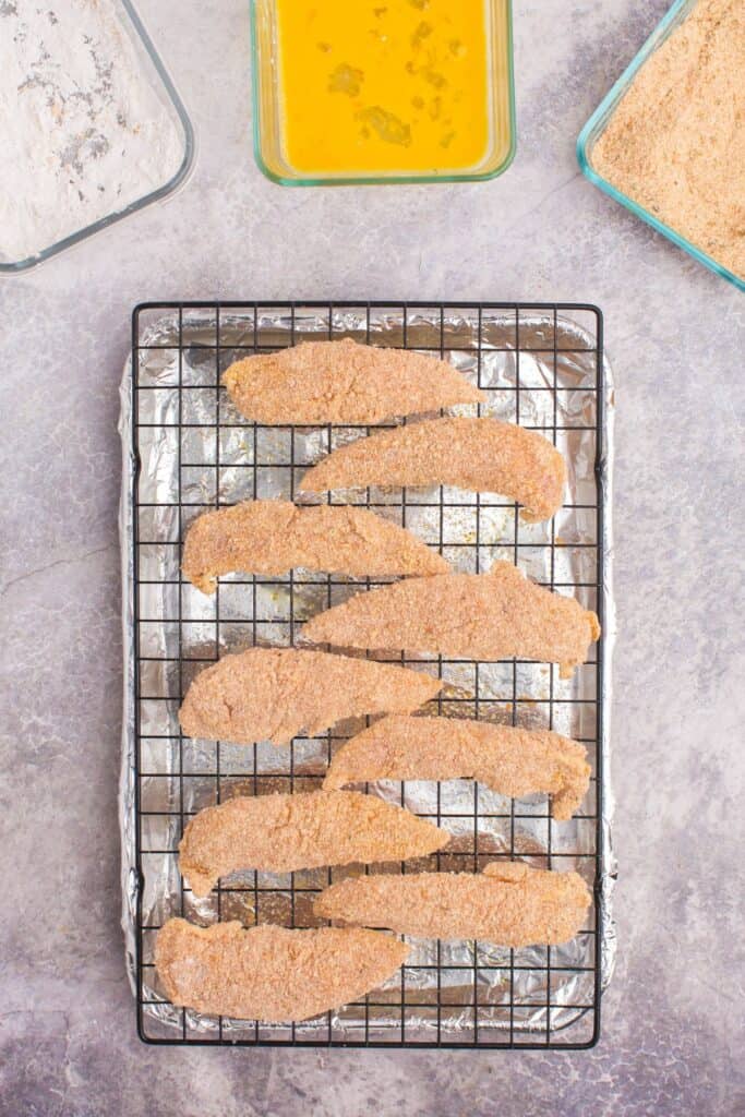 raw breaded chicken tenders on a baking sheet rack