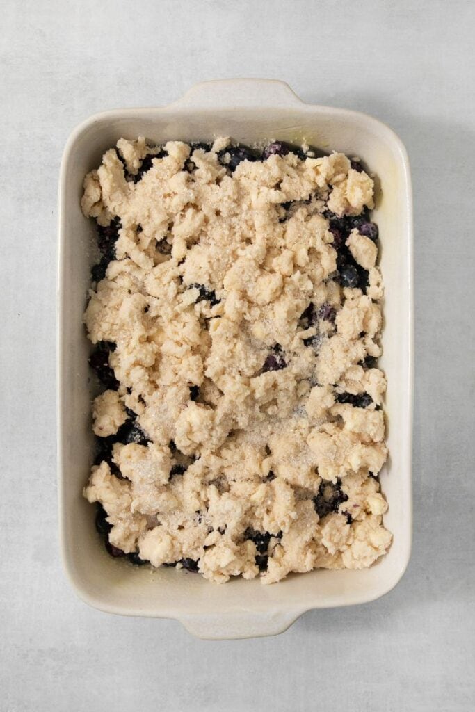 adding buttery crumble topping over blueberries