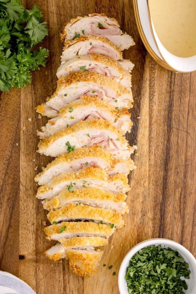 sliced chicken cordon bleu on a wooden cutting board with a dipping sauce