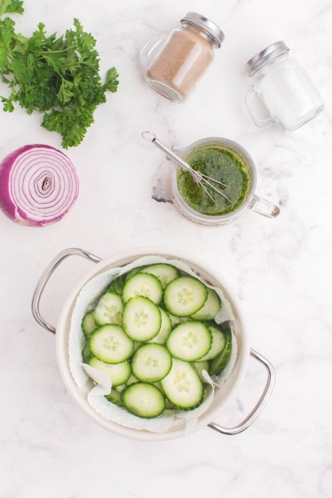 adding salted and sliced cucumbers to a white bowl