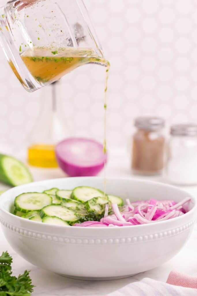 drizzling homemade dressing over the cucumber salad