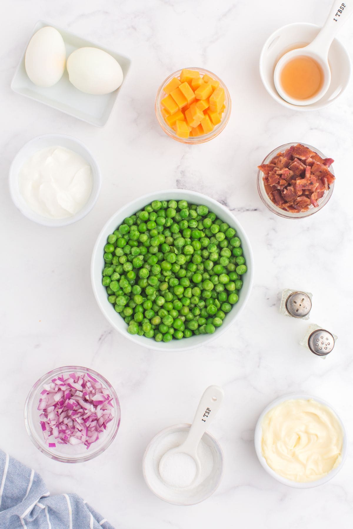 Ingredients needed to make pea salad: frozen peas, sour cream, mayo, bacon, eggs, onion, apple cider vinegar, cheddar cheese, salt, and pepper.